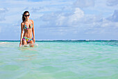 'A Woman Standing In The Ocean Wearing A Colourful Bikini And Sunglasses; Punta Cana, La Altagracia, Dominican Republic'