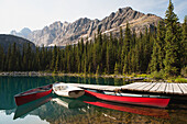 'Canoes and rowboat by a dock on a mountain lake with mountain range in background;Field british columbia canada'