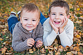 'Portrait of two young boys laying on the ground in fallen autumn leaves;St. albert alberta canada'