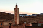 A tower in the midst of buildings with mountains in the background at sunset