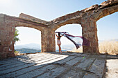 'A Woman Holding A Piece Of Sheer Fabric Behind Her As It Flows In The Wind Within Some Ruined Arches; Santa Barbara, California, United States Of America'