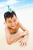 'A Boy Laying On The Sand At The Water's Edge With A Toy Whale On His Head; Kailua, Oahu, Hawaii, United States Of America'