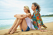 'A mother and daughter sitting together on the beach at the water's edge; Kauai, Hawaii, United States of America'