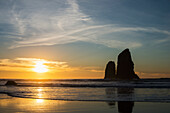 'The sunset with silhouettes of rock formations reflected in the wet sand; Cannon Beach, Oregon, United States of America'