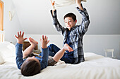 'Brothers having a pillow fight on a bed at home; Victoria, British Columbia, Canada'