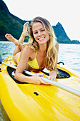 'A young woman in a yellow bikini laying on a stand up paddleboard; Kauai, Hawaii, United States of America'