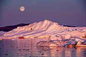 Vollmond über Fischerboot vor Eisbergen in der Dämmerung im Ilulissat-Eisfjord, Ilulissat, Kommune Qaasuitsup, Grönland