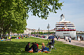 People enjoying a sunny Sunday afternoon in the park with cruise ship MS Deutschland (Reederei Peter Deilmann) moored along La Garonne river, Bordeaux, Gironde, Aquitane, France