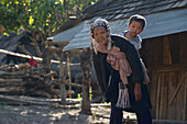Old Akha woman in traditional clothes smoking a pipe and carrying her grandchild on her back near Kyaing Tong, Kentung, Shan State, Myanmar, Burma