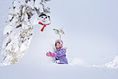Mädchen hockt neben einem Schneemann, Kreuzbergpass, Südtirol, Italien