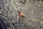 Junge hockt im Wasser in einem Steinbecken, Praia, Santiago, Kap Verde