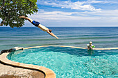 Father and son in a swimming pool, overflow pool, infinity pool, father diving into the water, header, jump, head dive, from tree, happiness, sea, tree, blue sky, luxury, paradise, family travel in Asia, parental leave, German, European, MR, Amed, Bali, I