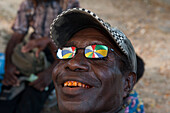 Reflection of a colourful umbrella in the sunglasses of a man with red teeth from chewing betelnut, Wewak, East Sepik Province, Papua New Guinea, South Pacific