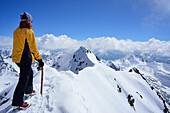 Female back-country skier at summit of Piz Buin and looking at mountain panorama, Silvretta Range, Lower Engadin, Engadin, Grisons, Switzerland