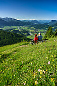 Zwei Personen sitzen auf einer Bank in einer Blumenwiese, Kaisergebirge, Inntal und Zillertaler Alpen im Hintergrund, Kranzhorn, Chiemgauer Alpen, Tirol, Österreich