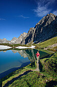 Woman hiking along lake Steinsee, Steinkarspitze and Schneekarlespitze in background, Lechtal Alps, Tyrol, Austria