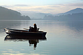 Eine Frau sitzt in einem Boot auf dem Edersee im Nationalpark Kellerwald-Edersee und liest ein Buch im Morgenlicht, Edersee, Nordhessen, Hessen, Deutschland, Europa