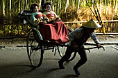 Zwei junge Geisha Frauen werden mit einem Rikscha Menschenkraftwagen durch einen Bambuswald gefahren, Kyoto, Region Kansai, Japan