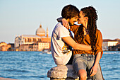 Young couple kissing on the banks of the Canale della Giudecca in Dorsoduro with Chiesa del Redentore church in the distance, Venice, Veneto, Italy, Europe