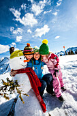Mother and two children in snow near a snowman, Planai, Schladming, Styria, Austria