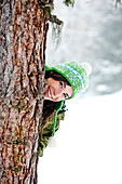 Junge Frau hinter einem Baum lacht in die Kamera