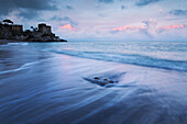 Beach and the sea with a fortress in the background, in the colours of sunset, Amalfitana coast, Campania