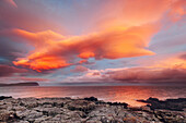 Rocky cliff with a view on the sea, with red clouds in the sunset, Skye's island, Scotland