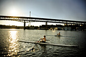 Two young men row single boats on lake Washington during sunset for Crew practice. Seattle, WA.