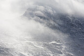 The rocky face of Mt. Washington in the White Mountains of New Hampshire, barely visible through thick, swirling clouds. Mt. Washington in New Hampshire is known for severe weather and home to the Mt. Washington Observatory.