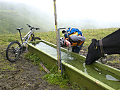 A mountain biker is drinking from a water tap for cows, on the way from First to Grindelwald.