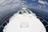 Fish eye view of the bow of a large white boat with  two men in the wheelhouse. navigating through clear waters under a blue sky with fluffy clouds in Costa Rica.