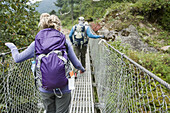A man and woman cross a metal man made suspension bridge on the trek to Mt. Everest base Camp.
