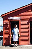 FIVE ISLANDS, MAINE, USA. A man holds freshly caught lobster outside his dockside food stand.