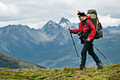 A woman with a backpack trekking with the Darwin Mountain range in the background in Tierra del Fuego,  Patagonia,  Chile.