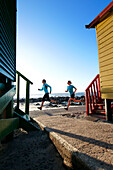 Katrin Schneider and Susann Scheller running past the famous and colorful bathing huts in St.James near Muizenberg. Cape Town, South Africa.