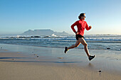 Susann Scheller running along Bloubergstrand beach in Cape Town with a perfect view of Table Mountain in the back. Cape Town, South Africa.