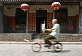 Old Chinese man riding a bike in front of a traditional old street building of Pingyao. Shaanxi Province. China