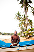 A young man sits in his boat on a sunny day on a beach.