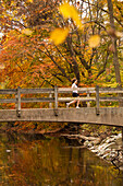 A woman runs over a bridge on a wooded trail in Rock Creek Park in Washington DC under Autumn leaves.