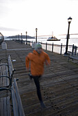 A man running on a dock in the harbour of San Francisco at sunrise with the Oakland Bay Bridge in the background. California, USA.  Lars Schneider / Aurora Photos 