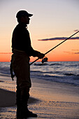 Fisherman casts from the shore at sunset on  Cape Cod National Seasohore outside of Provincetown, Massachusetts.