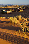 Wolwedans Dune Lodge chalets glow in early moring light. The chalets are surrounded by the burnt orange dunes of the Namib Rand Nature Reserve, Namibia.