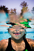 A young girl poses for the camera half underwater in a pool.