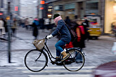A biker makes her way through the streets of Copenhagen, Denmark at dusk.  Danes love their bicycles and commute to work throughout the year on them regardless of the weather.  With long stretches of cold gray weather throughout the winter and a wet bitin
