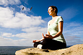 Eine Frau am Strand, die Yoga und Meditation praktiziert.