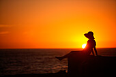 A woman sits in a wall as the sun sets over the Pacific Ocean in Baja, Mexico.