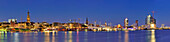 Panorama of Hamburg with view over the river Elbe to illuminated St. Pauli-Landungsbruecken with Pegelturm, Heinrich-Hertz-Turm, Telemichel, museum ship Rickmer Rickmers, churches St. Michaelis, Nicolai and Katharinen, Hamburg, Germany