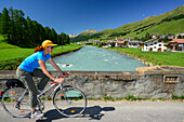 Cyclist passing a bridge crossing Inn river, S-chanf, La Plaiv, Upper Engadin, Canton of Graubuenden, Switzerland