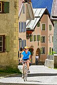 Radfahrerin fährt über Kopfsteinpflaster, Guarda, Unterengadin, Engadin, Kanton Graubünden, Schweiz