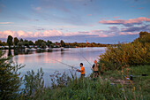 Two fishermen on the banks of the Main river with camp site at sunset, Volkach, Franconia, Bavaria, Germany